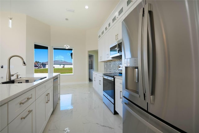 kitchen featuring decorative backsplash, white cabinets, marble finish floor, stainless steel appliances, and a sink