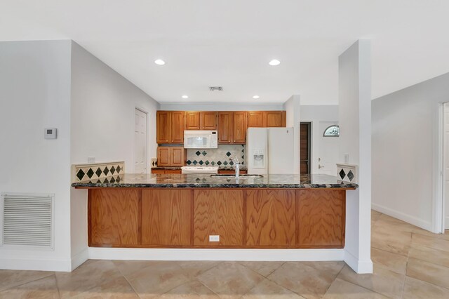 kitchen featuring dark stone counters, white appliances, visible vents, and a peninsula