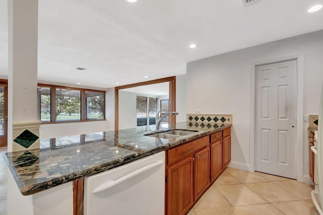 kitchen featuring dark stone counters, a peninsula, white dishwasher, and brown cabinets