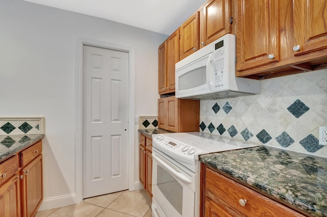 kitchen featuring light tile patterned floors, white appliances, backsplash, brown cabinets, and dark stone countertops