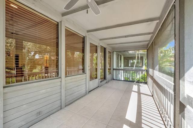 unfurnished sunroom with a ceiling fan and beamed ceiling