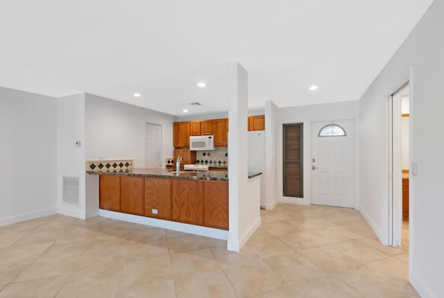 kitchen featuring visible vents, brown cabinetry, dark stone counters, white appliances, and a peninsula