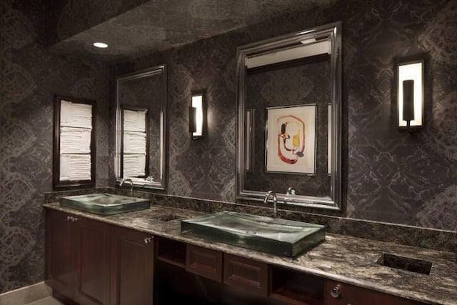 bathroom with wallpapered walls, a sink, and double vanity