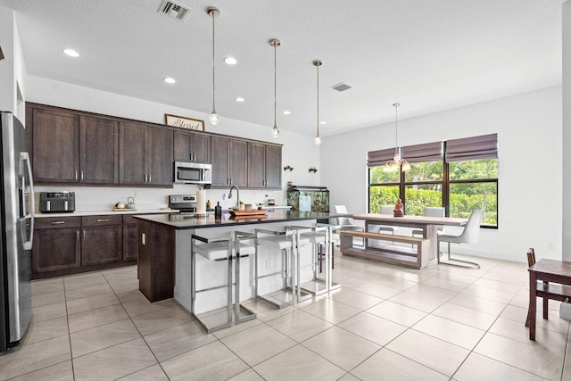 kitchen featuring a center island, decorative light fixtures, stainless steel appliances, dark countertops, and visible vents