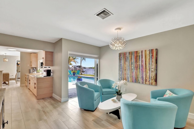 living area featuring visible vents, light wood-style flooring, baseboards, and an inviting chandelier