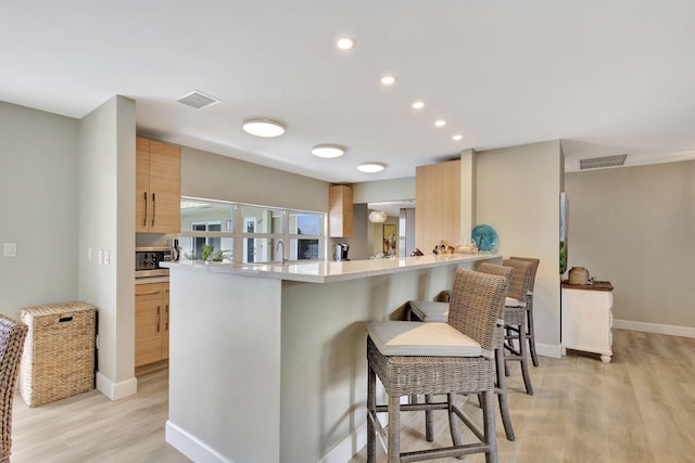 kitchen with baseboards, visible vents, light wood-style flooring, a breakfast bar, and light countertops