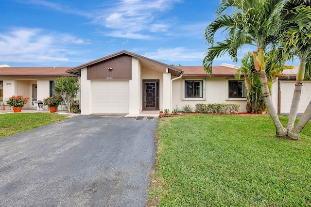 single story home with a garage, aphalt driveway, a front lawn, and stucco siding