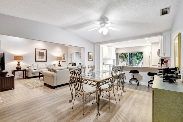 dining room with visible vents, light wood-style flooring, vaulted ceiling, a textured ceiling, and ceiling fan