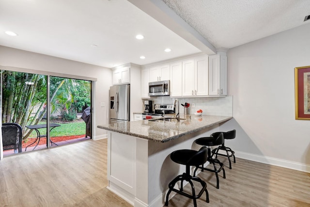 kitchen featuring stone counters, tasteful backsplash, appliances with stainless steel finishes, white cabinetry, and a sink