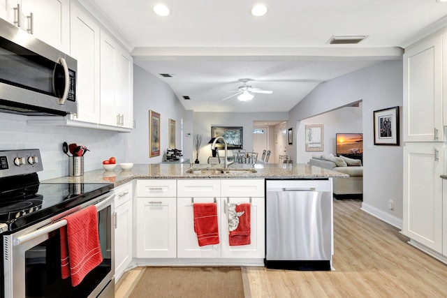 kitchen featuring a peninsula, a sink, white cabinets, open floor plan, and appliances with stainless steel finishes