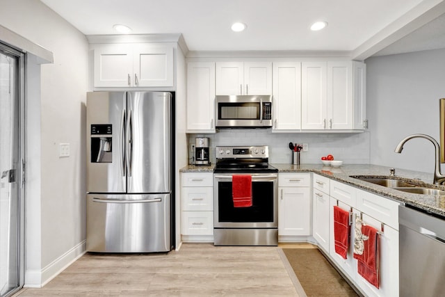 kitchen featuring stainless steel appliances, white cabinetry, a sink, and light stone countertops