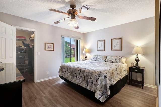 bedroom with a textured ceiling, dark wood finished floors, baseboards, a closet, and a walk in closet