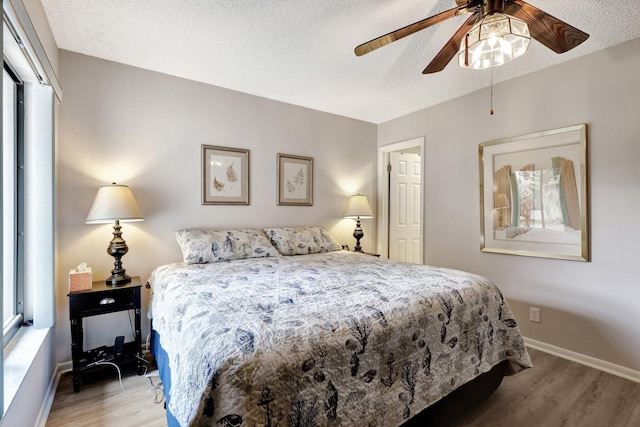 bedroom featuring light wood-style floors, a textured ceiling, baseboards, and a ceiling fan