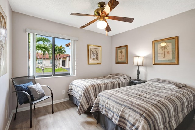 bedroom with baseboards, a textured ceiling, a ceiling fan, and light wood-style floors