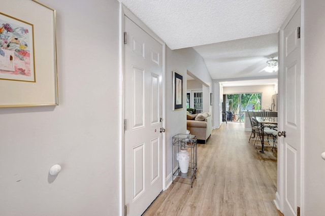 corridor with light wood-style floors and a textured ceiling