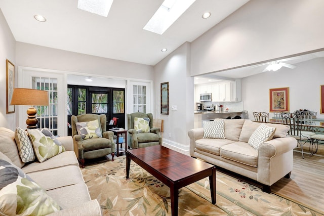 living room featuring high vaulted ceiling, recessed lighting, a skylight, baseboards, and light wood-type flooring