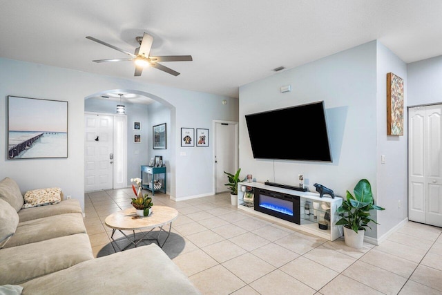 living area featuring a ceiling fan, arched walkways, baseboards, and light tile patterned floors