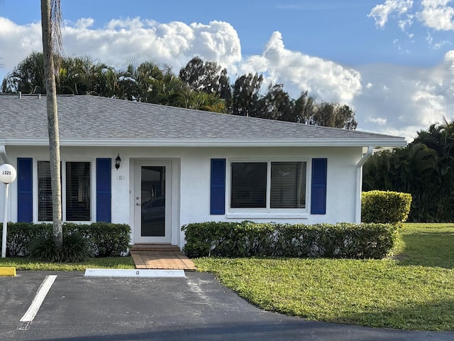 ranch-style house with uncovered parking, a front lawn, roof with shingles, and stucco siding