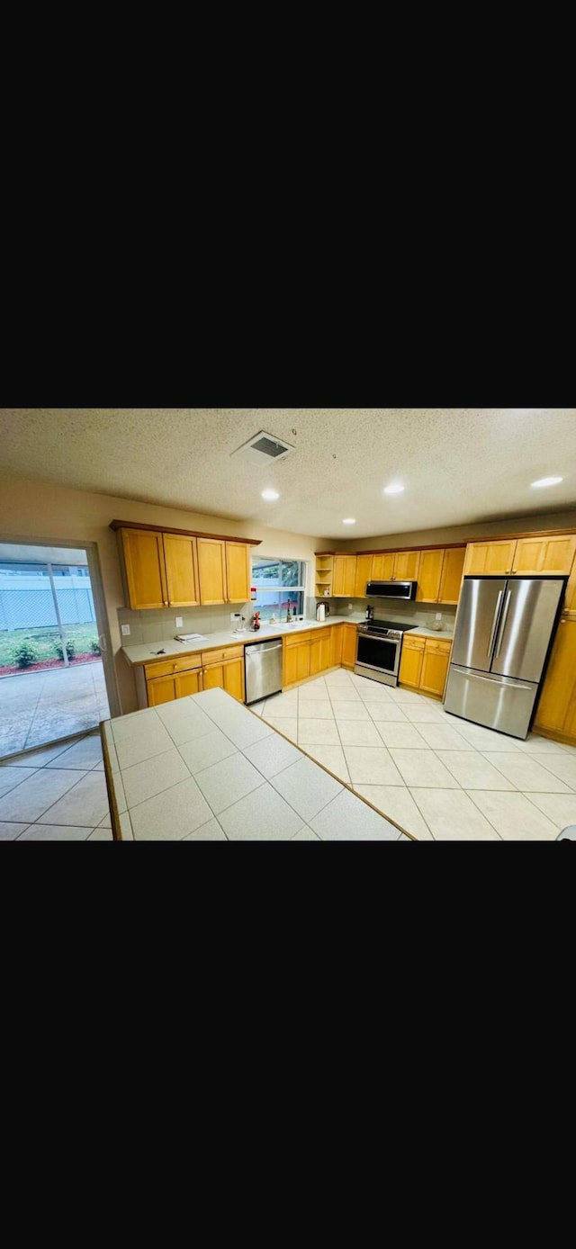 kitchen featuring visible vents, tile countertops, ventilation hood, stainless steel appliances, and a textured ceiling