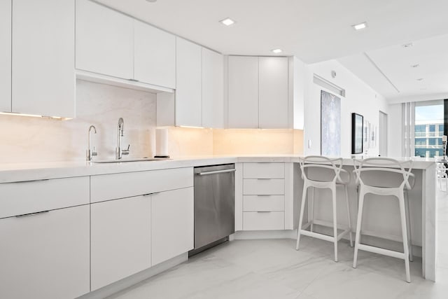 kitchen featuring light countertops, a sink, backsplash, and a kitchen bar