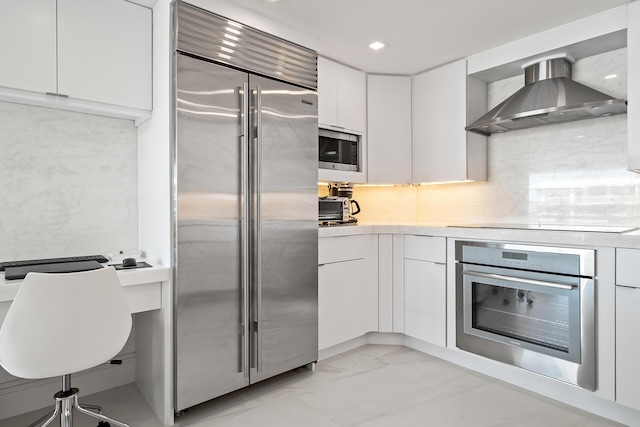 kitchen with light countertops, white cabinets, wall chimney range hood, modern cabinets, and built in appliances