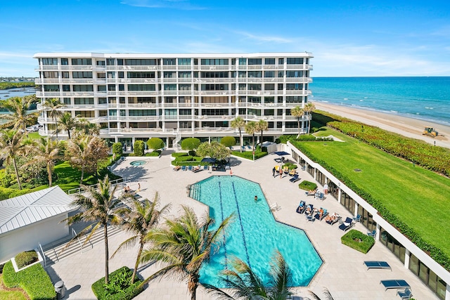 pool with a patio, a water view, and a view of the beach