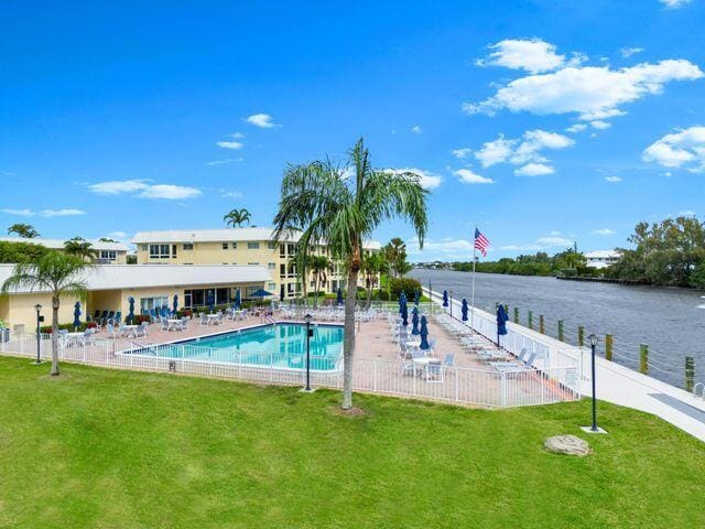pool featuring fence, a lawn, a water view, and a patio