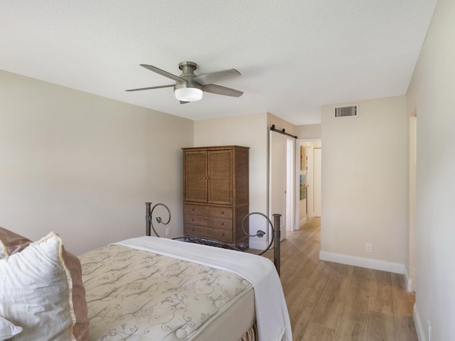 bedroom featuring a barn door, light wood-type flooring, ceiling fan, baseboards, and visible vents