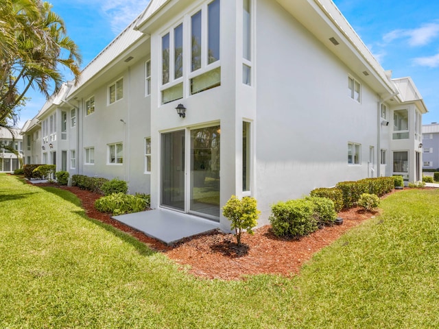 rear view of property featuring a lawn and stucco siding
