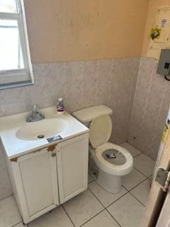 bathroom featuring wainscoting, toilet, tile patterned flooring, vanity, and tile walls