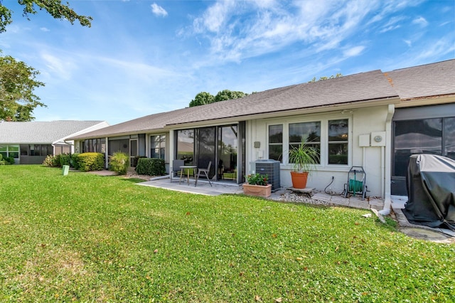 back of property featuring a lawn, a patio, a sunroom, roof with shingles, and central air condition unit