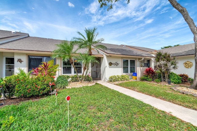 ranch-style house with a shingled roof, a front lawn, and stucco siding