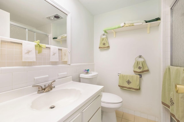 bathroom featuring toilet, a shower with door, tile patterned flooring, vanity, and tile walls