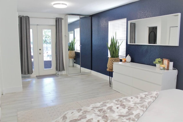 foyer entrance with french doors, a textured wall, baseboards, and wood finished floors