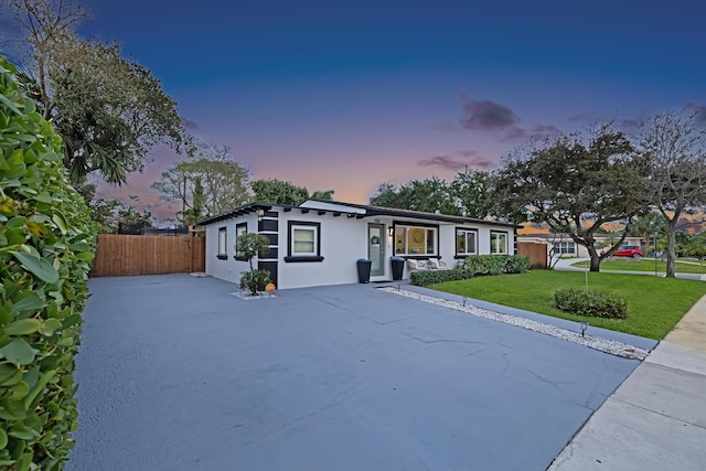 view of front of house with fence, a lawn, and stucco siding