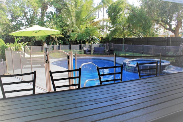 view of swimming pool featuring a pool with connected hot tub, fence, and a deck