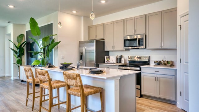 kitchen with light countertops, appliances with stainless steel finishes, a kitchen island with sink, and gray cabinetry