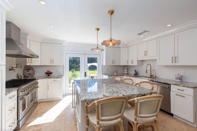 kitchen with appliances with stainless steel finishes, white cabinets, decorative light fixtures, and wall chimney range hood