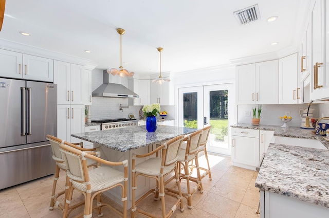 kitchen with high end refrigerator, visible vents, white cabinets, wall chimney exhaust hood, and a center island