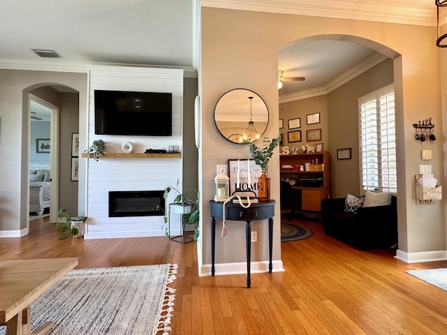 living room with hardwood / wood-style floors, ornamental molding, a large fireplace, ceiling fan, and baseboards