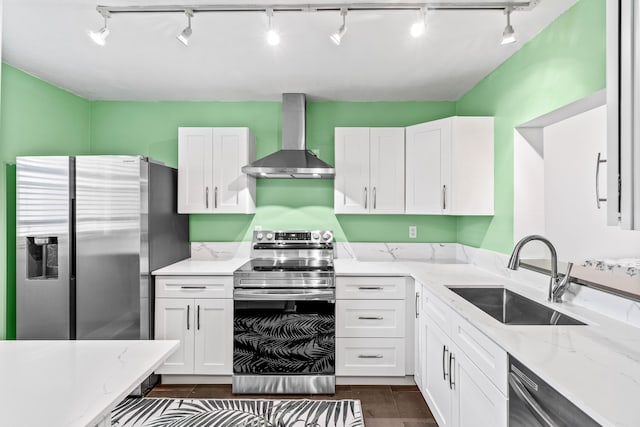 kitchen featuring stainless steel appliances, white cabinetry, a sink, wall chimney range hood, and light stone countertops