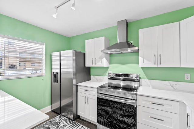 kitchen with light stone counters, stainless steel appliances, white cabinetry, baseboards, and wall chimney exhaust hood