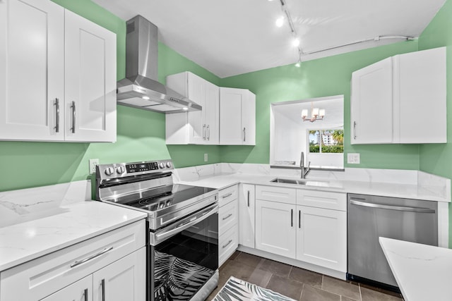 kitchen featuring light stone counters, stainless steel appliances, wall chimney range hood, white cabinetry, and a sink