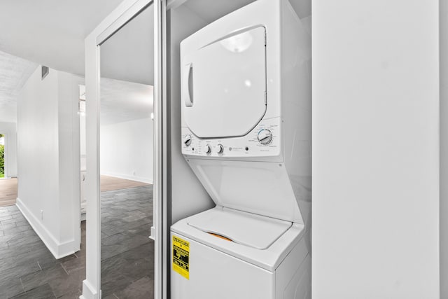 laundry area featuring stacked washer and dryer, dark wood-type flooring, laundry area, visible vents, and baseboards