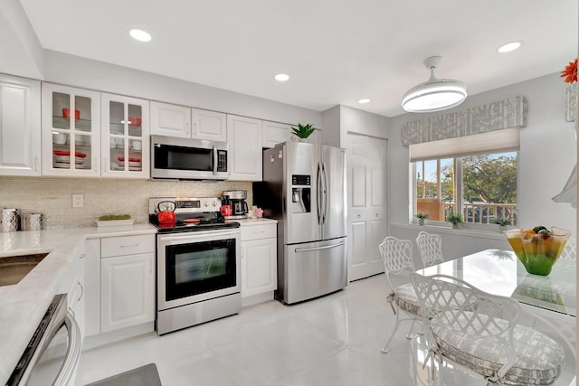 kitchen featuring appliances with stainless steel finishes, white cabinets, glass insert cabinets, and tasteful backsplash