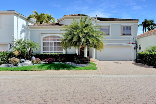 view of front facade featuring an attached garage, a tile roof, decorative driveway, and stucco siding