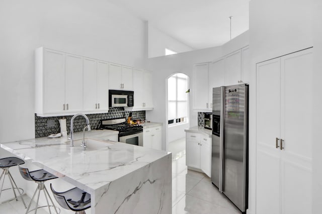 kitchen featuring tasteful backsplash, arched walkways, a peninsula, stainless steel appliances, and a sink