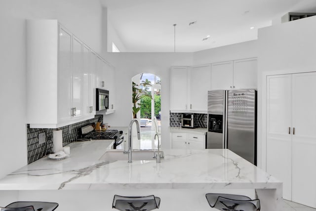 kitchen featuring a peninsula, stainless steel fridge, white cabinetry, and range with gas cooktop