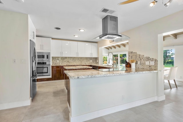 kitchen with visible vents, a peninsula, appliances with stainless steel finishes, a wealth of natural light, and island range hood