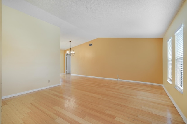 spare room with a textured ceiling, lofted ceiling, a notable chandelier, baseboards, and light wood-style floors